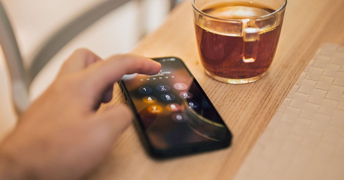A hand unlocking a smartphone on a wooden table next to a glass mug of tea