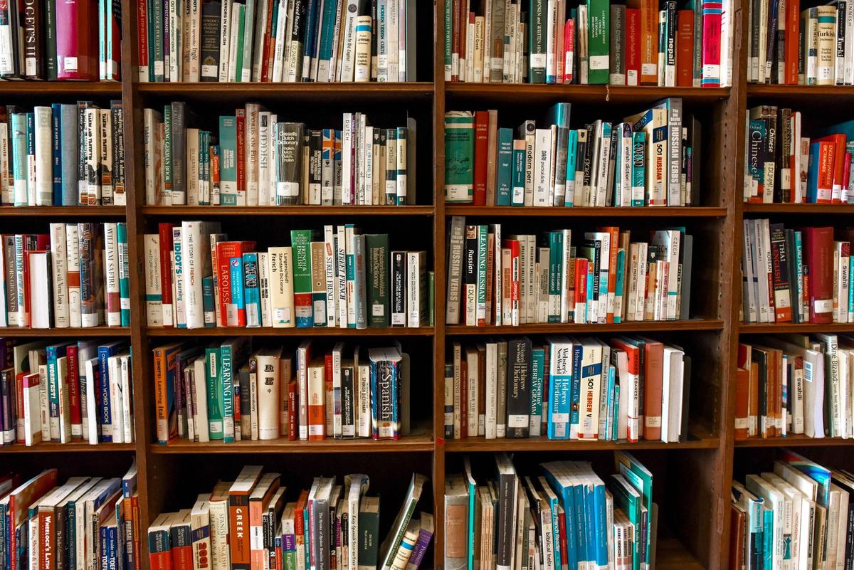 Wooden bookshelves in a library filled with books, grouped into sections by subject
