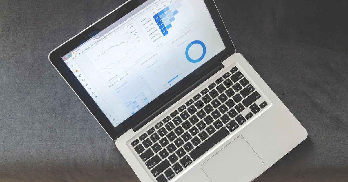 An open silver laptop on a dark grey surface, its screen showing an analytics dashboard with a line chart, a bar chart and a ring chart