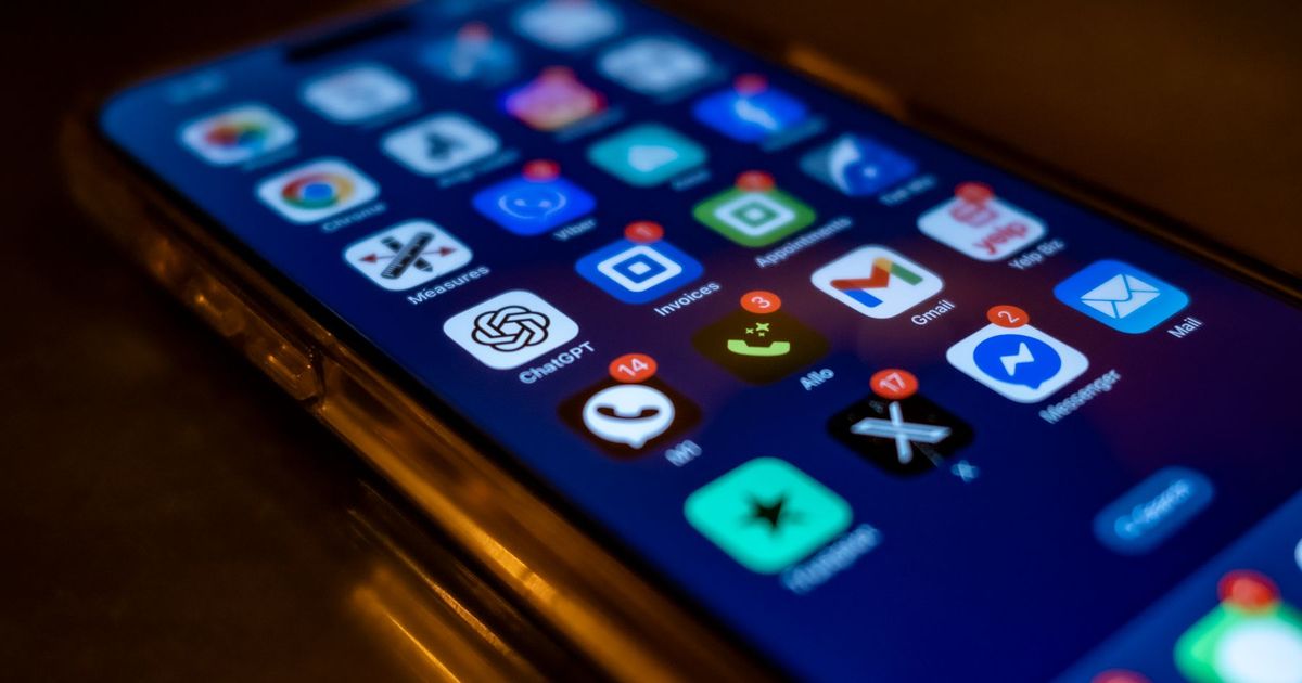 An iPhone lying on a dark table, its home screen full of app icons with red notification badges