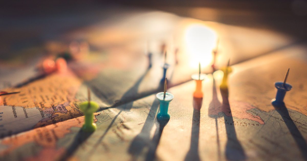 Colorful push pins standing on a world map in warm low sunlight, casting long shadows across the paper