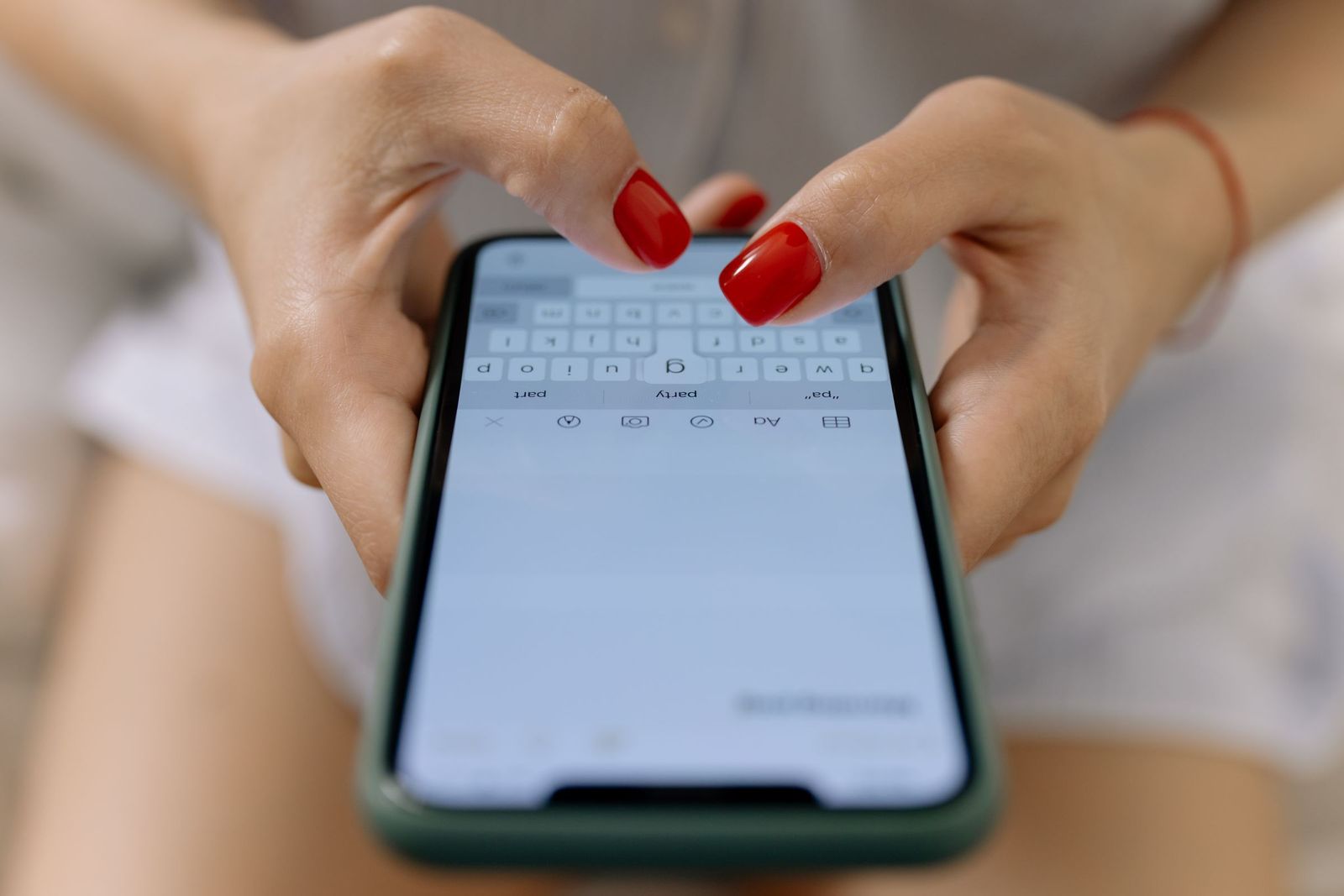 Two hands with red nails typing on a smartphone keyboard
