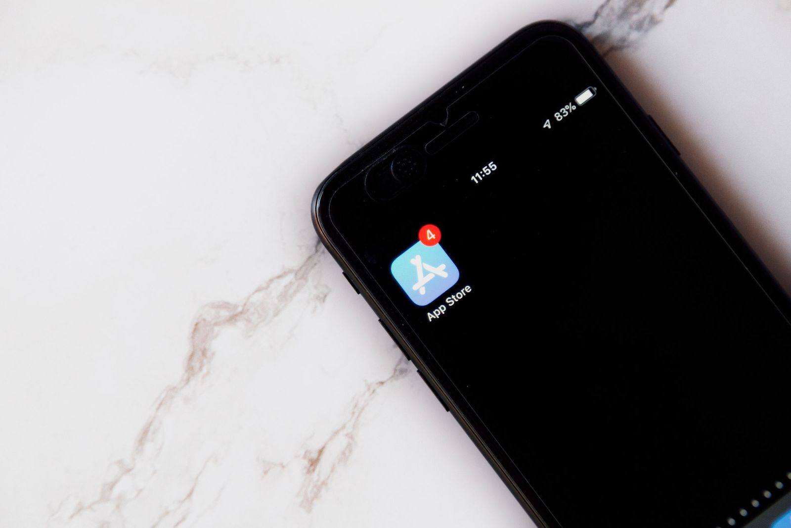 An iPhone on a white marble surface showing the blue App Store icon with a red notification badge