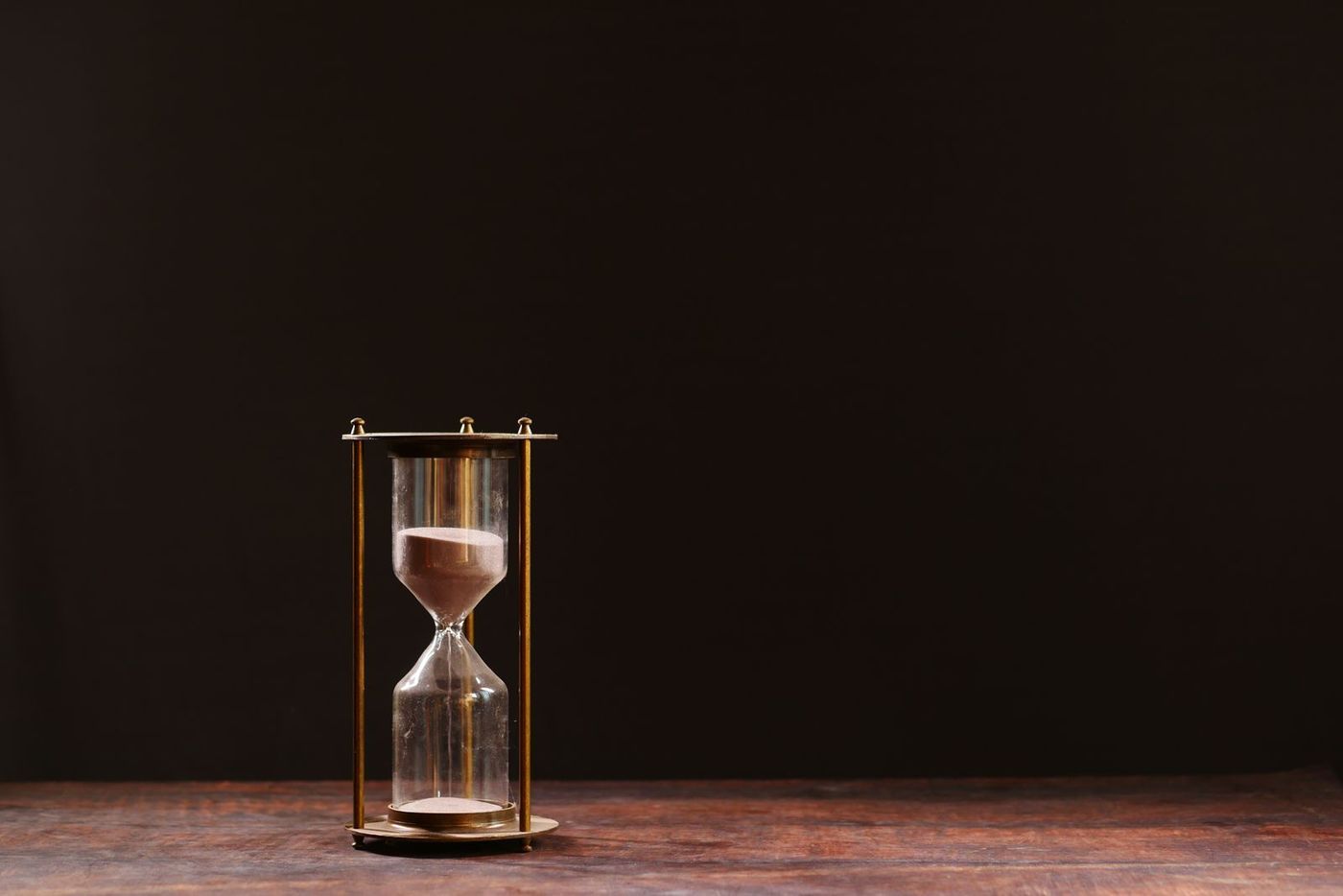 An hourglass with sand falling, on a wooden surface against a dark background