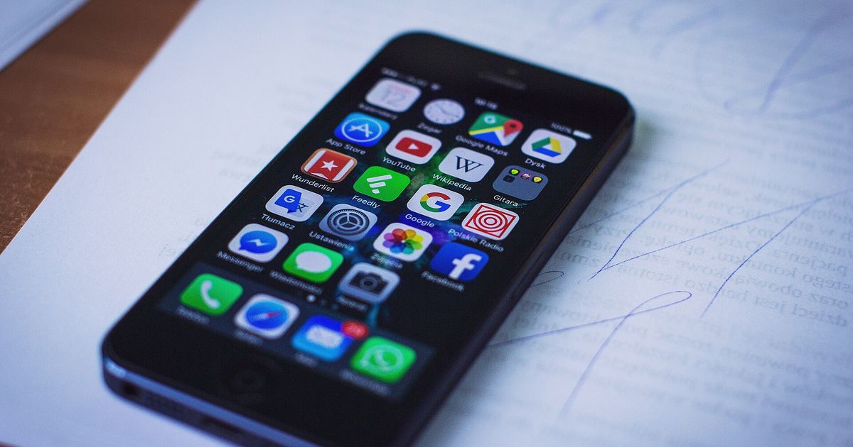 An iPhone lying on a handwritten page, its home screen showing the App Store icon in the top row beside YouTube, Google Maps and Wikipedia