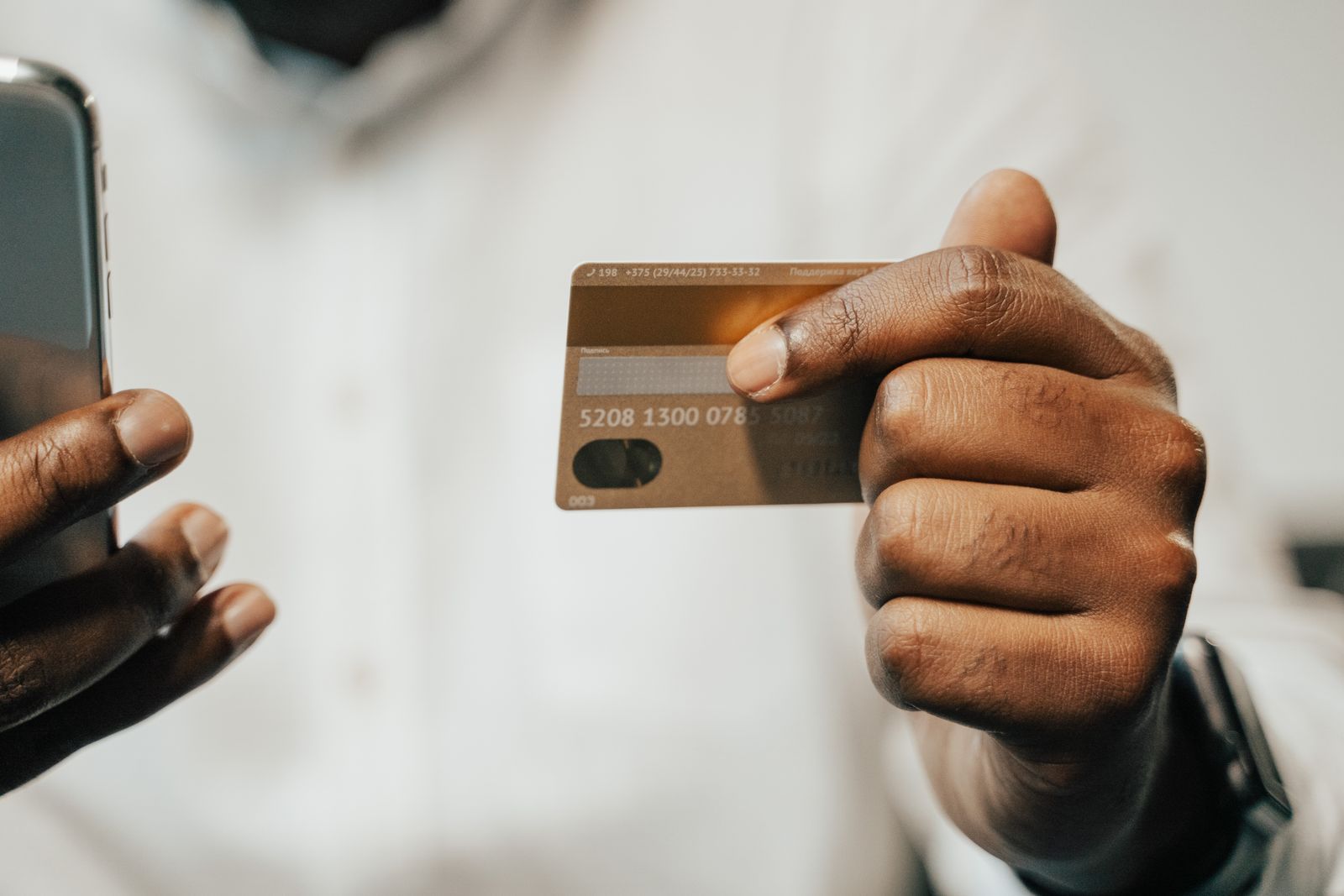 A person holding a phone in one hand and a bank card in the other