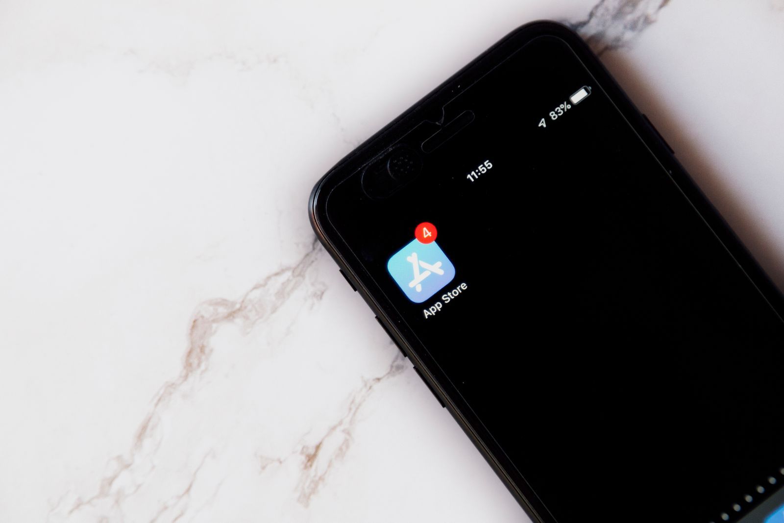 An iPhone on a white marble surface with only the App Store icon on its screen, showing a red badge with the number 4