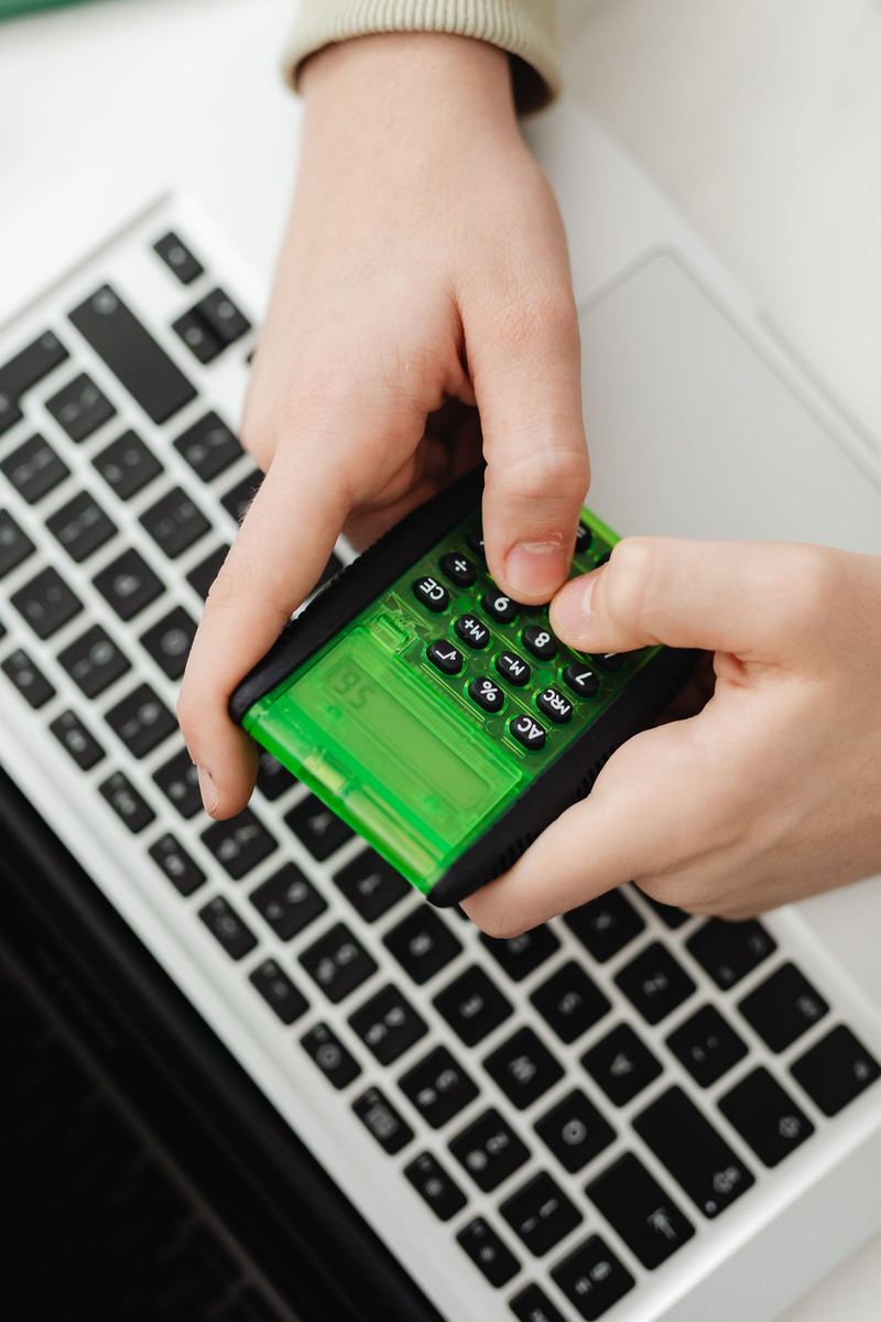 Two hands using a green calculator over a laptop keyboard