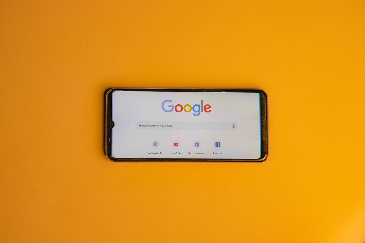 A smartphone on a bright yellow background showing the Google search home page
