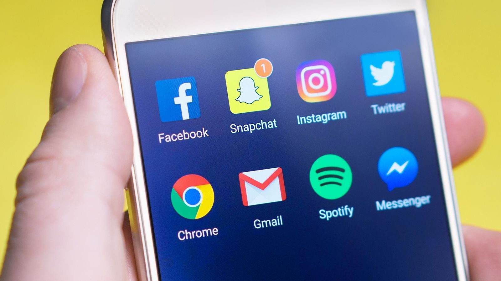 A hand holding an Android phone with a home screen of app icons on a dark background