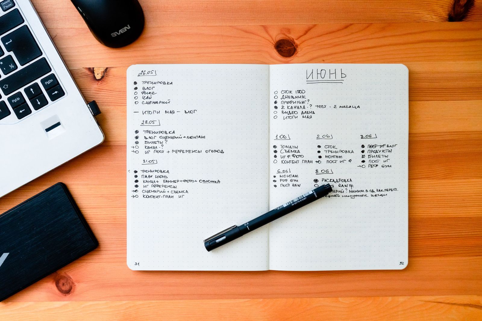 An open notebook with handwritten dated notes and a pen beside a laptop on a wooden desk