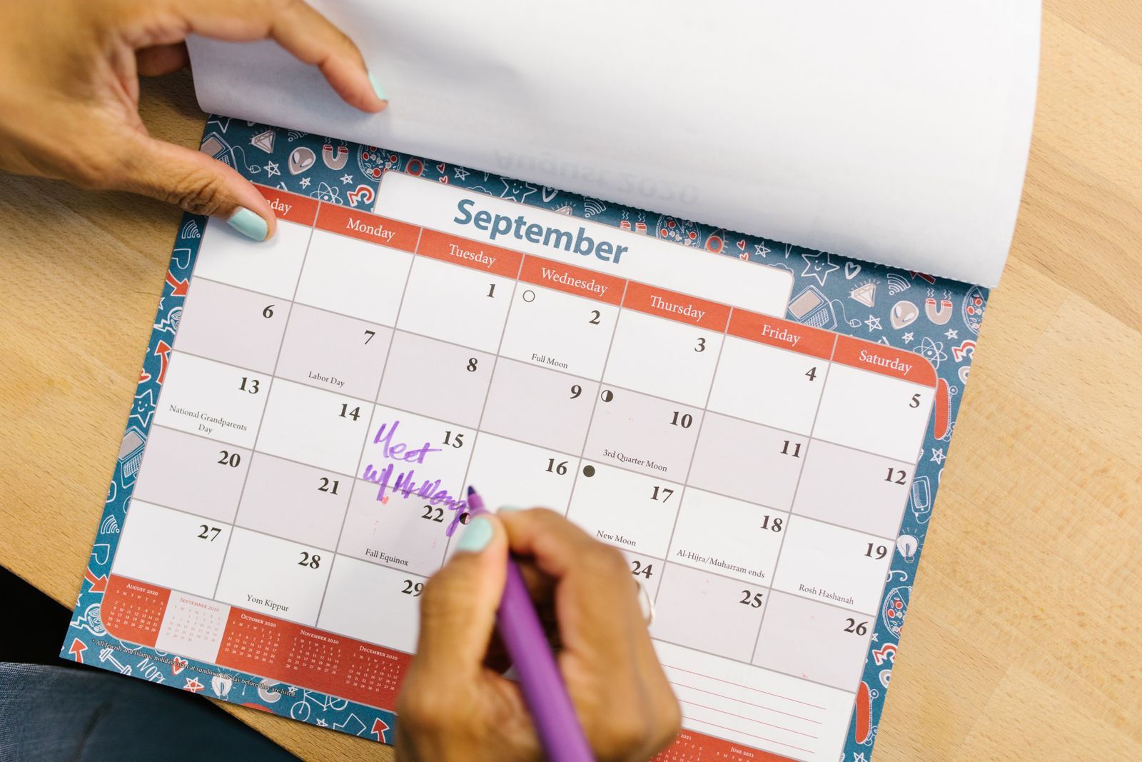 A hand marking a date on a September page of a desk calendar with a purple pen