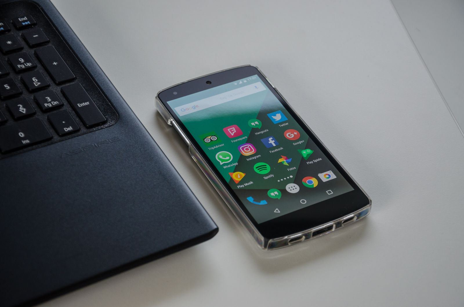 An Android phone with a home screen of app icons lying beside a laptop keyboard