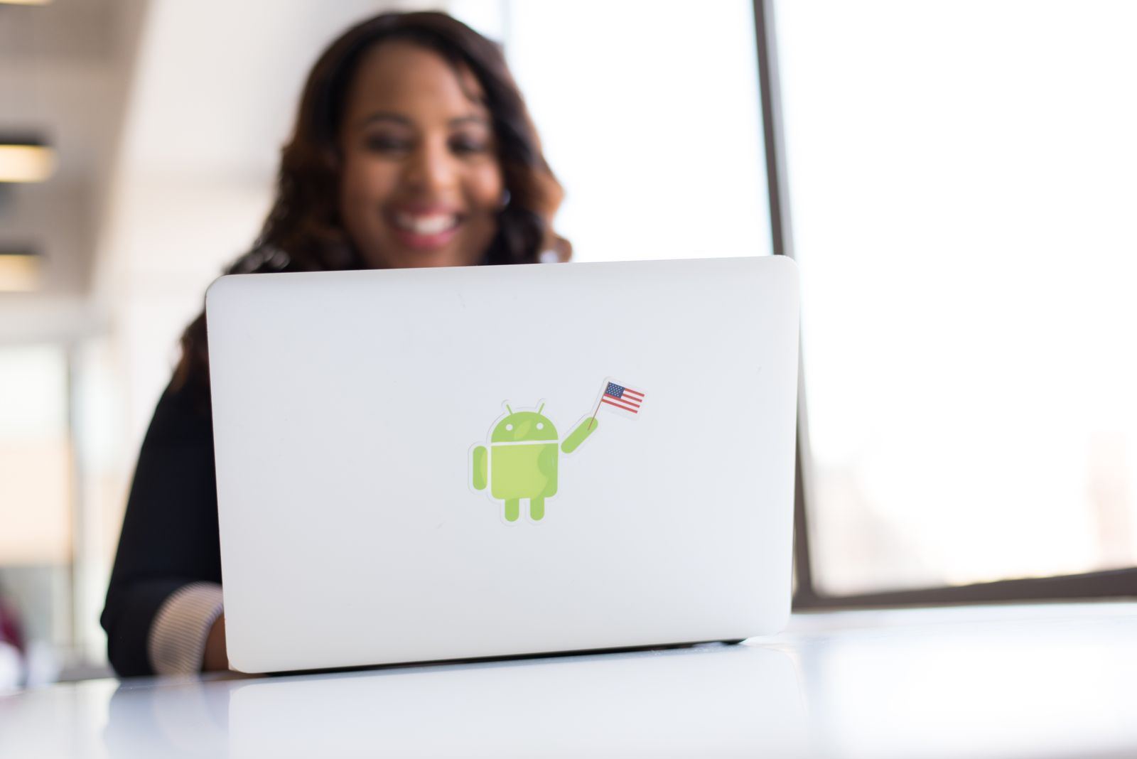 A developer smiling at a laptop with an Android robot sticker on its lid