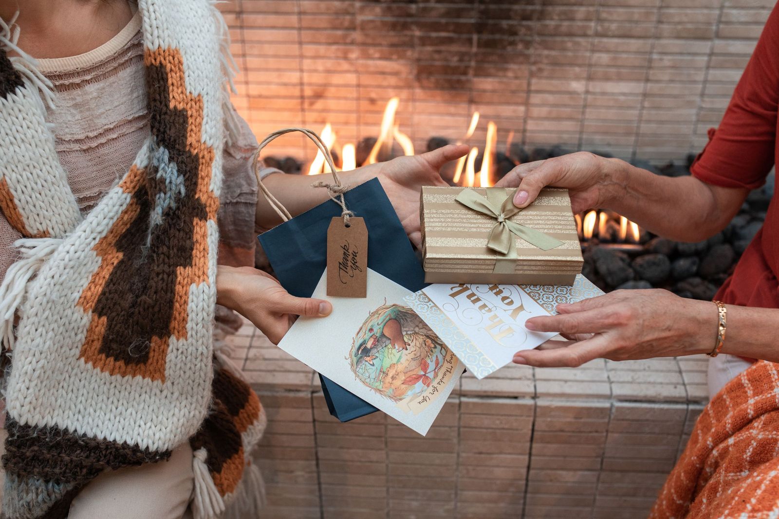 Two people exchanging a wrapped gift and cards in front of a fireplace