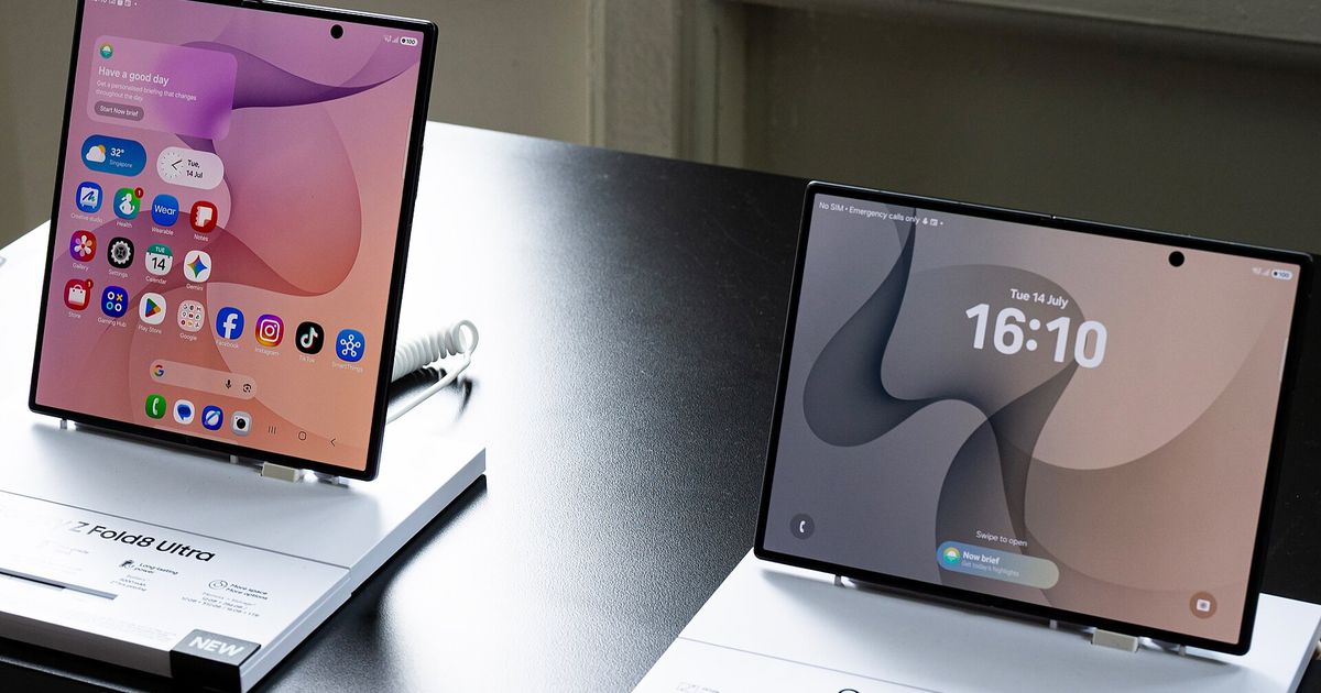 Two unfolded book-style foldable phones on white display stands in a shop, one showing a home screen of app icons and the other a lock screen reading 16:10