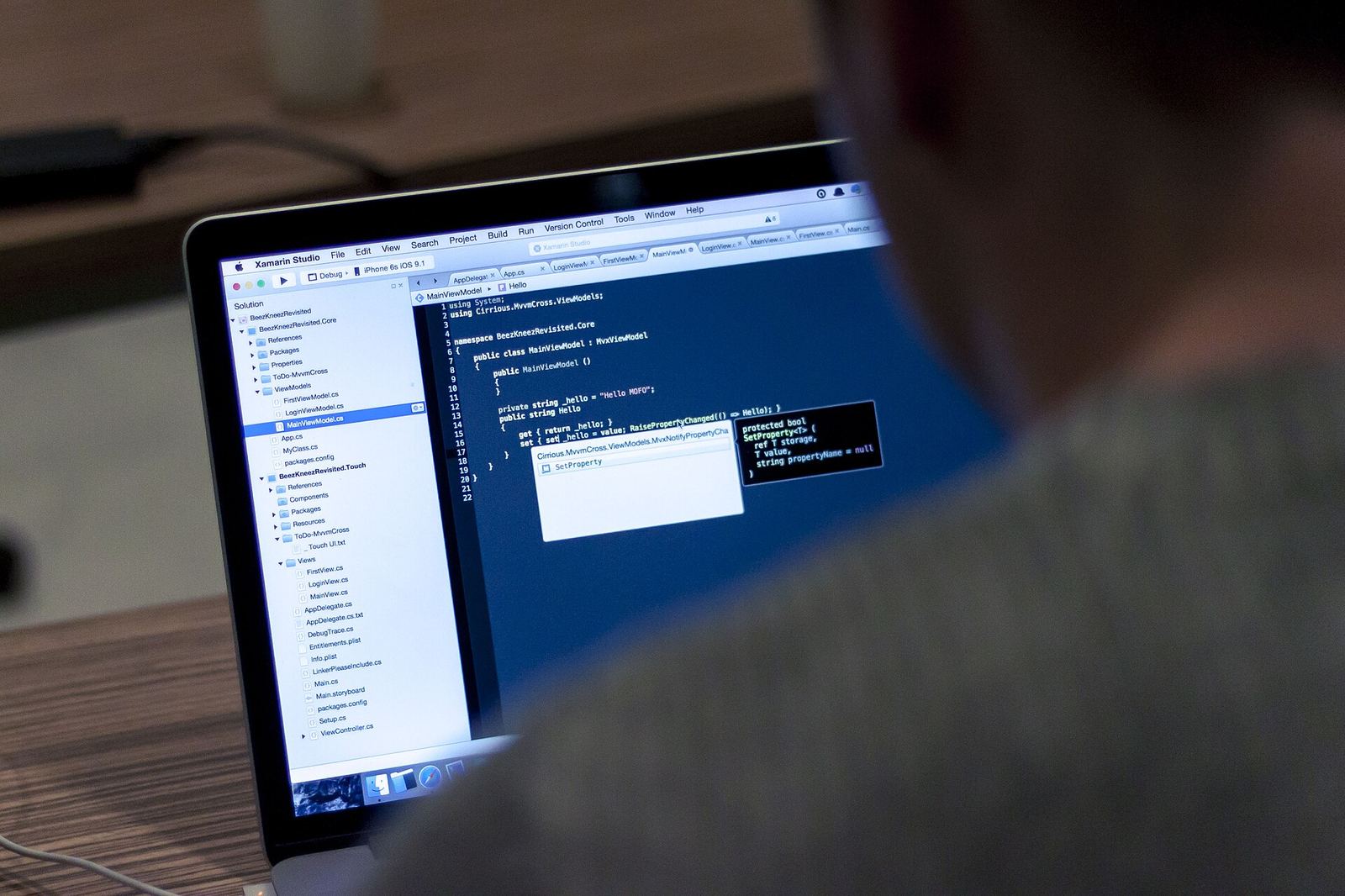 A developer working at a MacBook with an IDE open, the project tree on the left and an iPhone build target selected in the toolbar