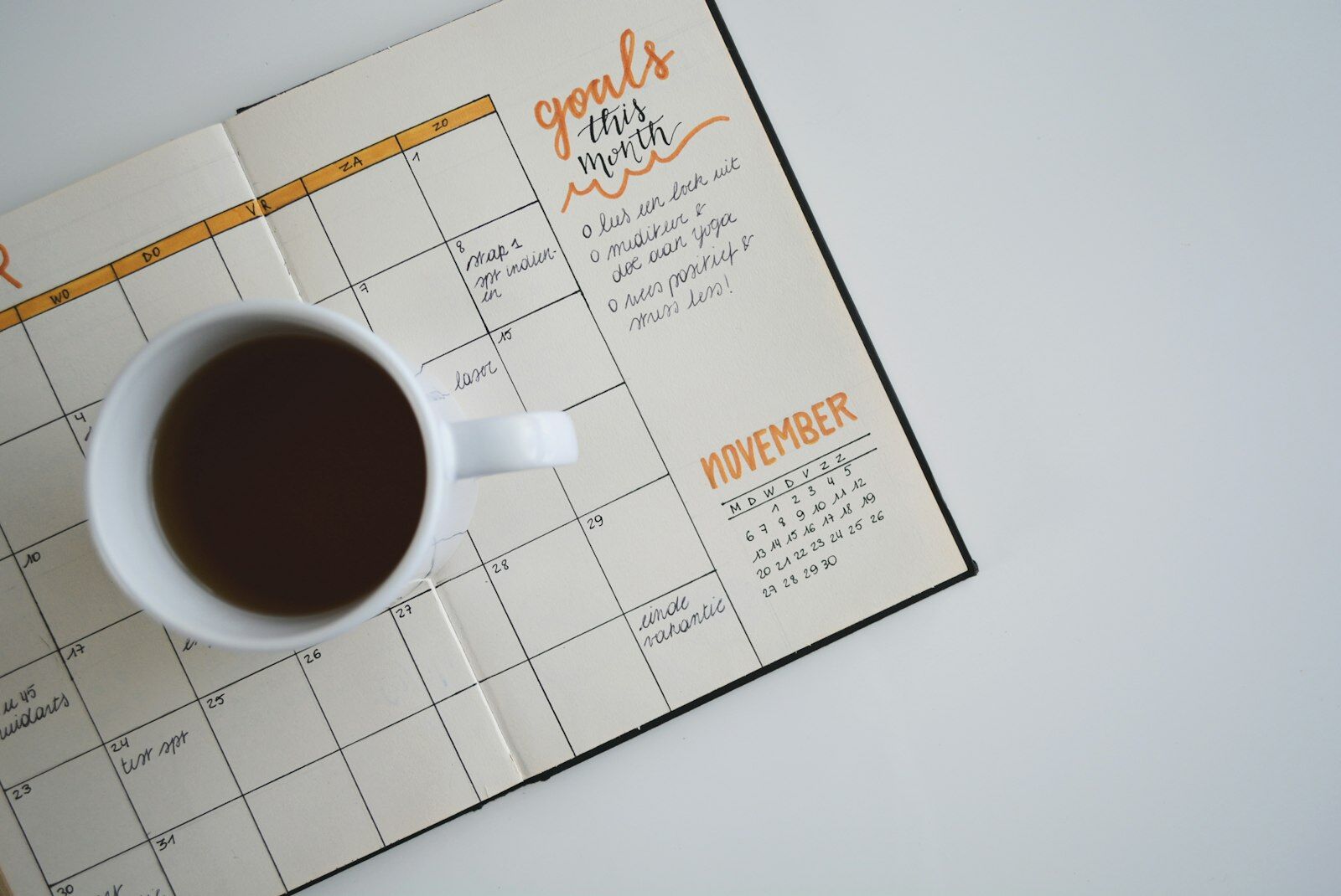 An open monthly planner with a hand-lettered "goals this month" list and a November calendar, a cup of black coffee resting on the grid