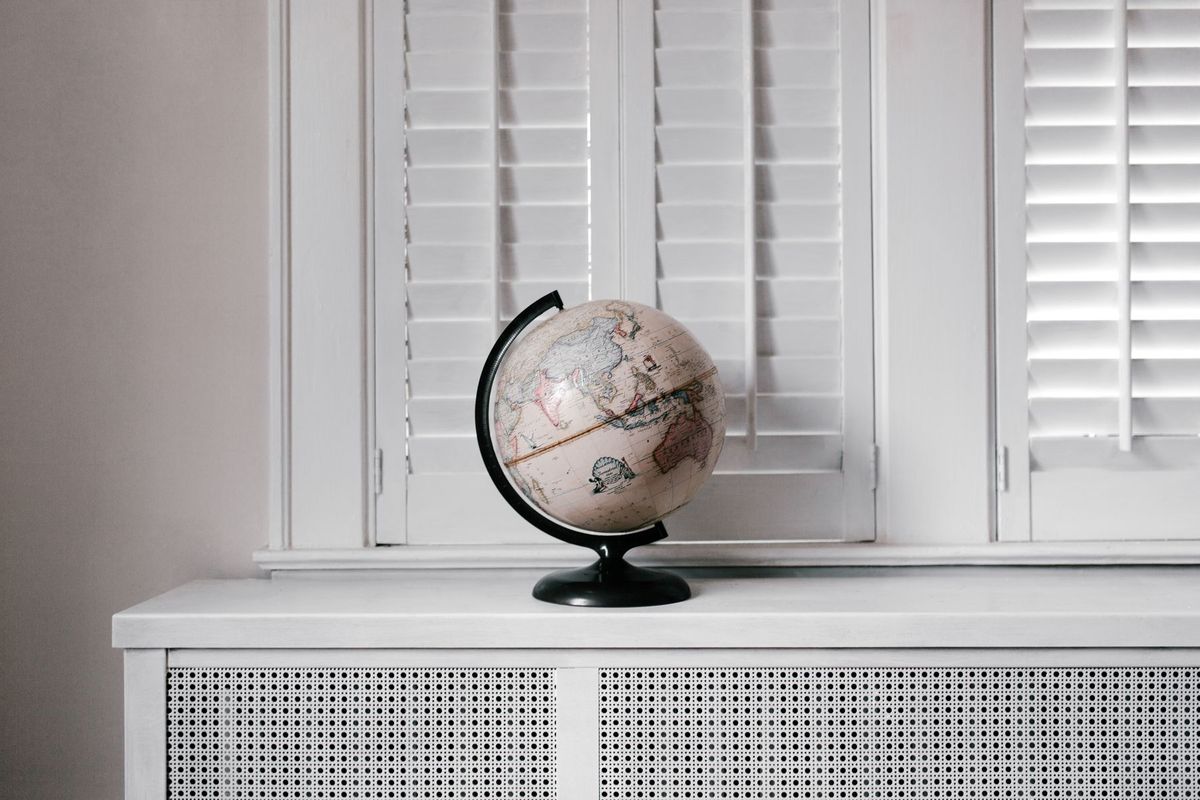 A white and black desk globe on a windowsill in front of closed white shutters
