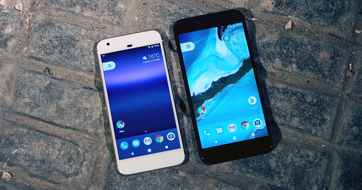 Two Google Pixel phones, one white and one black, lying side by side on grey paving stones with their Android home screens lit