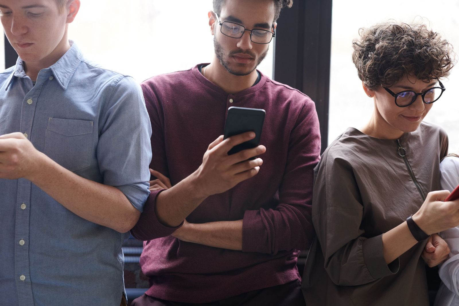 A group of young people sitting side by side, each looking at their own smartphone