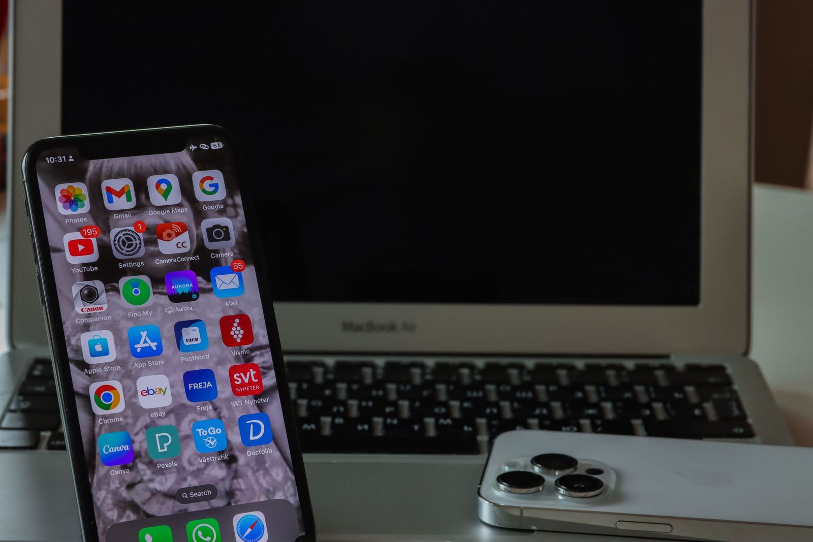 An iPhone showing its home screen propped up beside a laptop keyboard