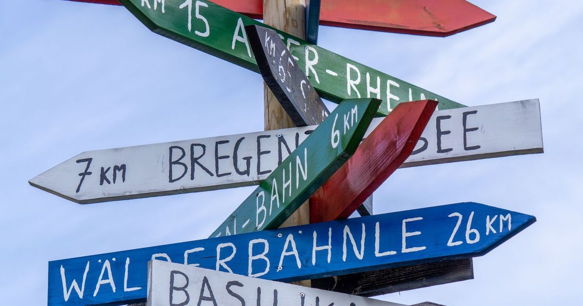 A wooden signpost against a blue sky crowded with colourful arrow signs pointing in different directions