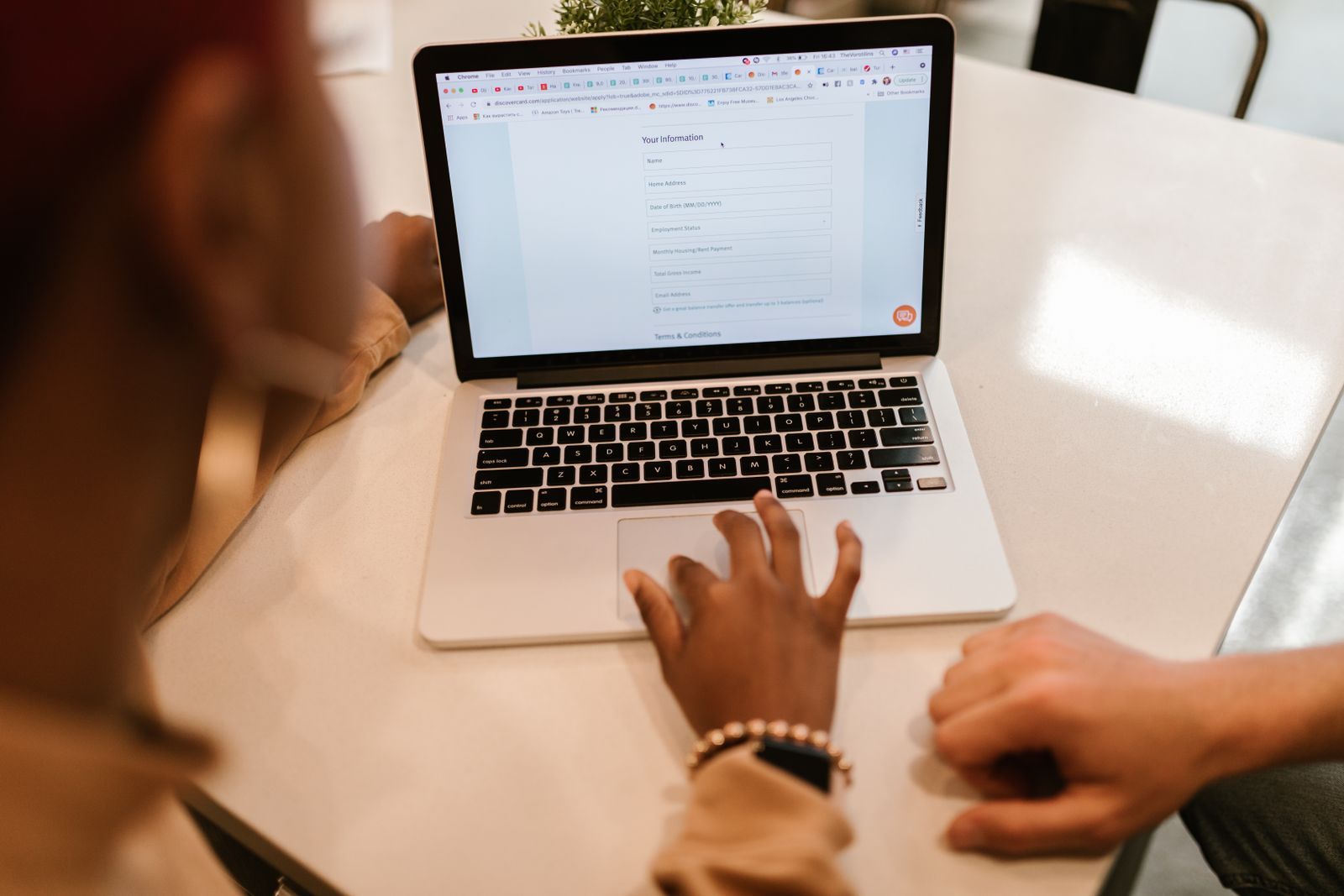 Two people at a desk, one typing into an online form on a laptop
